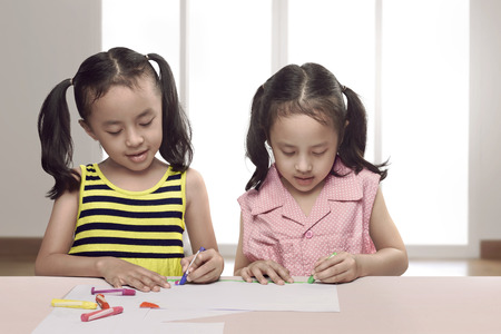 Portrait of two asian little girl draw on sheet of paper in the homeの写真素材