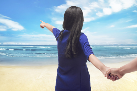 Portrait asian couple traveler holding hand and pointing at the ocean blueの写真素材