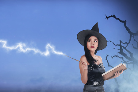 Pretty asian witch woman wearing hat and using her spell with misty backgroundの写真素材