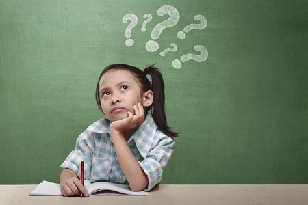 Funny expression asian little girl thinking something with chalkboard backgroundの写真素材