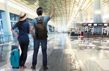 Excited asian couple traveler pointing with hand in the airportの写真素材