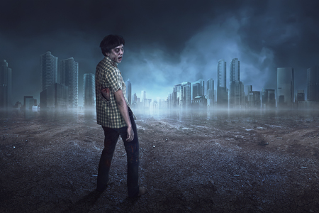 Spooky asian zombie man in clothes standing on the dark cityの写真素材