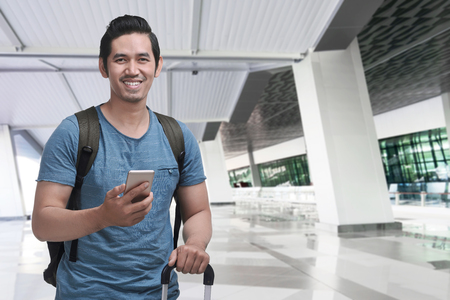 Cheerful asian traveler with backpack using cellphone on the airportの写真素材