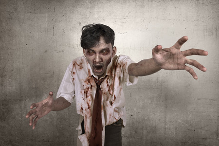 Creepy and bloody asian zombie man reaching to you against dirty wall backgroundの写真素材