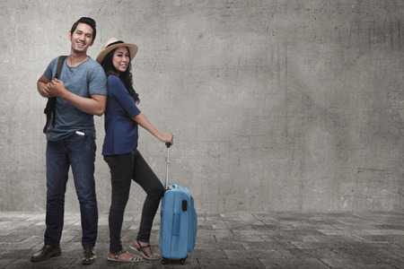 Young asian couple tourist with luggage waiting flight over grunge backgroundの写真素材