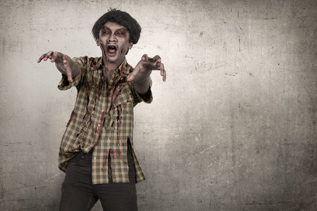Portrait of asian zombie man with hand to reach you over grunge backgroundの写真素材