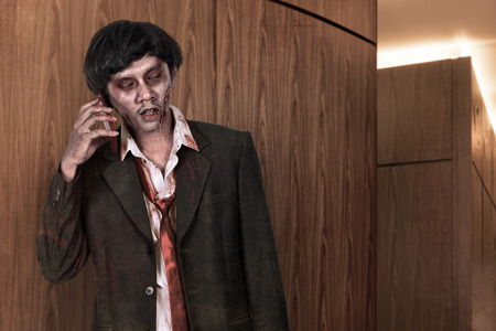 Portrait of creepy asian zombie man in suit call via cellphoneの写真素材