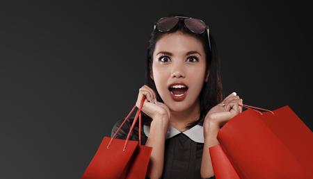 Happy asian woman with red shopping bag celebrating Black Friday over black backgroundの写真素材