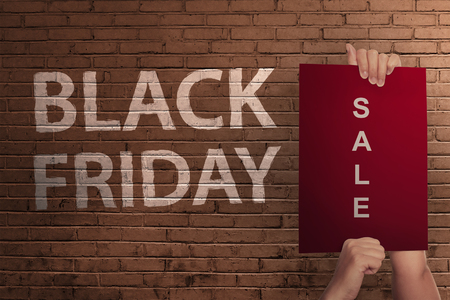 Black Friday text with hand holding sale banner against wall backgroundの写真素材