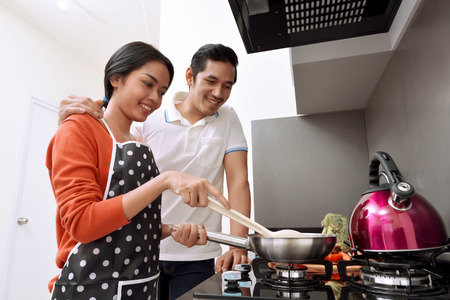 Portrait of asian couple smiling and cooking together in the kitchenの写真素材