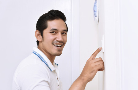 Handsome asian man turning off the light with wall switch in the homeの写真素材