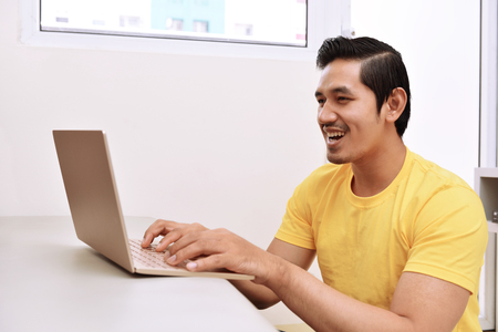 Happy asian man sitting with laptop in the living roomの写真素材