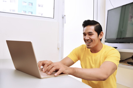 Happy asian man sitting with laptop in the living roomの写真素材
