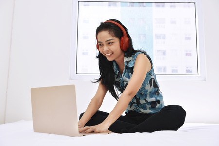 Happy asian woman using laptop and enjoying the music on bedroomの写真素材