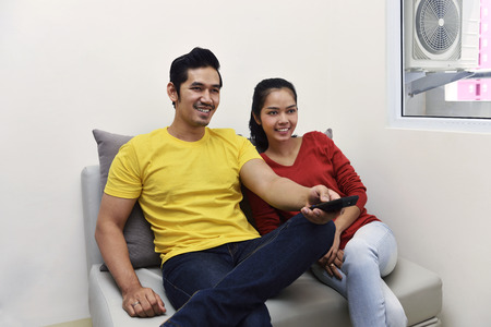 Portrait of asian couple enjoying watching television together at homeの写真素材