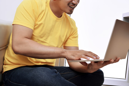 Happy asian man with laptop sitting on the couch at homeの写真素材