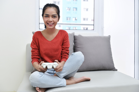 Beautiful asian woman with games controller playing video games on the couchの写真素材