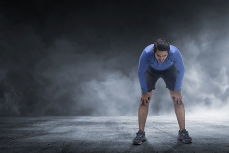 Young asian runner man taking rest from jogging on the concrete floorの写真素材
