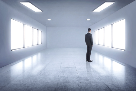 Portrait of young asian businessman looking through window from white roomの写真素材