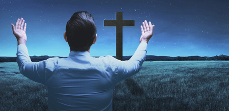 Back view of man raising hand while praying to god over night backgroundの写真素材
