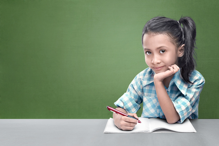 Smiling asian little girl doing her homework against chalkboard backgroundの写真素材