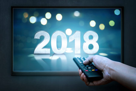 Hand holding remote control with 2018 on TV screen. Happy New Year 2018