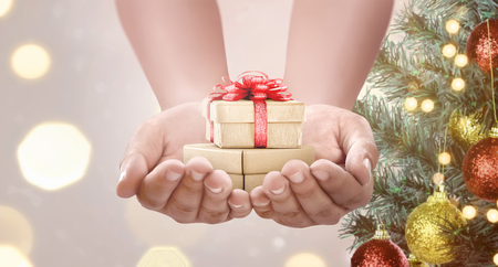 Human hand holding gift box with christmas tree decoration over blurred light backgroundの写真素材