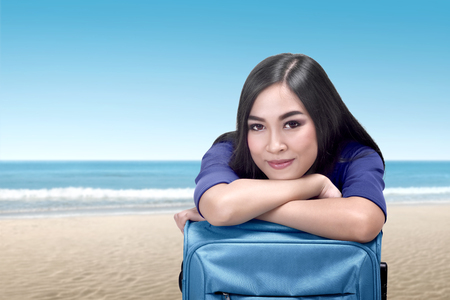 Young asian woman lean back on suitcase relaxing on the beachの写真素材