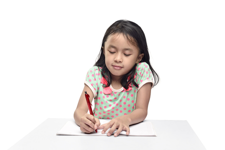 Portrait of asian little girl with pen writing in the book posing isolated over white backgroundの写真素材