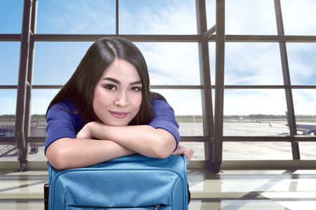 Smiling asian woman with suitcase waiting flight departure in the airportの写真素材