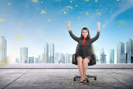 Excited asian business woman sitting on armchair in the rooftop with skyscrapers backgroundの写真素材