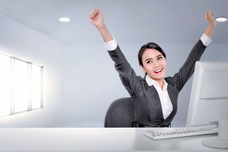Excited asian business woman with arms up while working on the officeの写真素材