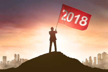 Silhouette of businessman hold a red flag with 2018 number on top mountain at sunset backgroundの写真素材