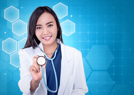 Young asian doctor woman in a white coat with stethoscope against abstract backgroundの写真素材