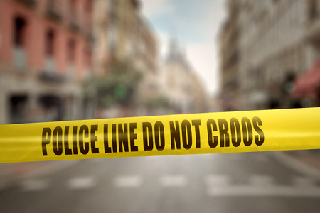 Yellow police line tape with text Police Line Do Not Cross against blurred city backgroundの写真素材