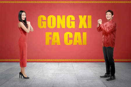 Happy chinese couple in cheogsam clothes with Gong Xi Fa Cai text on red wall background. Happy Chinese New Yearの写真素材