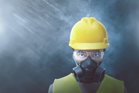 Young asian worker with yellow helmet and protective mask over black backgroundの写真素材