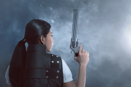Back view of Asian woman with police uniform holding guns on dark backgroundの写真素材