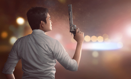 Back view of Asian man in police uniform holding guns with blurred light backgroundの写真素材