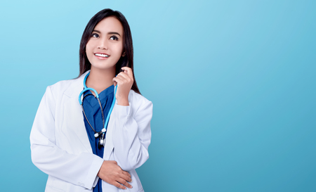 Young asian doctor woman in white coat and stethoscope over blue bright backgroundの写真素材