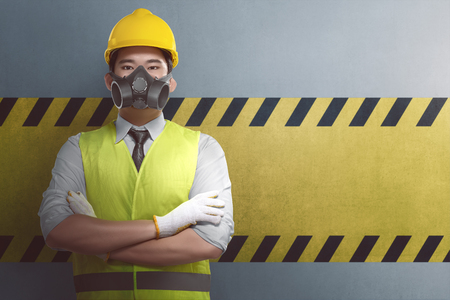 Young asian construction worker with crossed arm standing against yellow striped on the wallの写真素材