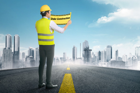 Back view of asian construction worker holding under construction signs in the roadの写真素材