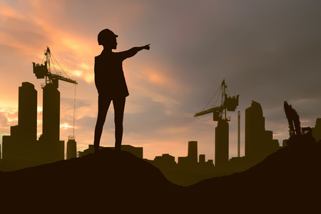 Silhouette of engineering woman with hard hat pointing project construction site at sunset backgroundの写真素材
