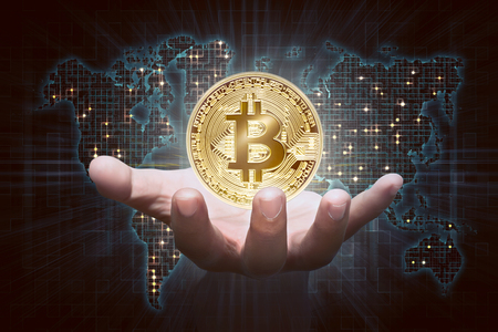 Man hands showing golden bitcoin as virtual money on digital world map backgroundの写真素材