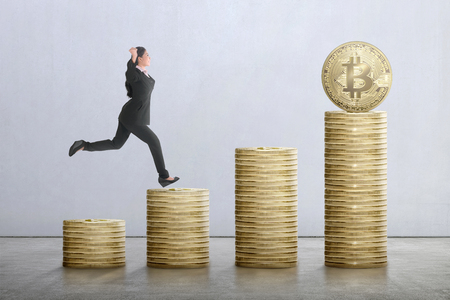 Happy asian business woman running on the stairs from bitcoin stack over gray wall backgroundの写真素材