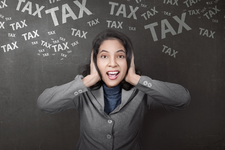 Stressful asian businesswoman with tax sign on black wall backgroundの写真素材