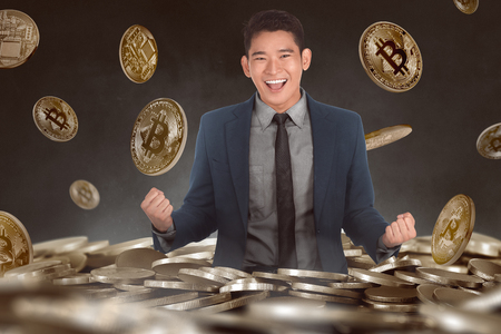 Excited asian businessman standing on bitcoin pile with over black backgroundの写真素材