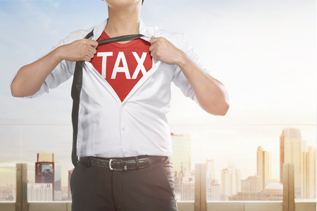 Businessman showing Tax text under his shirt with cityscape backgroundの写真素材