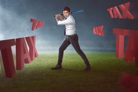 Portrait of asian businessman with baseball bat ready to hit tax text. Taxation conceptの写真素材