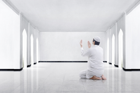 Back view of asian muslim man kneeling and praying to god in the mosqueの写真素材